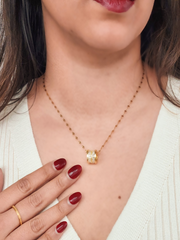 Gold necklace with a diamond pendant worn by a person with red nail polish.