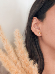 Close-up of an ear wearing a gold stud earring with pampas grass in the foreground.