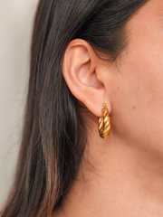 Close-up of a person wearing gold hoop earrings with a neutral background